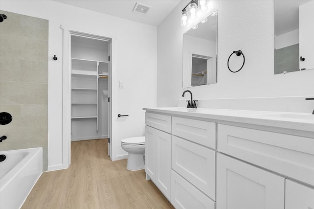 full bathroom featuring hardwood / wood-style flooring, vanity, tiled shower / bath combo, and toilet