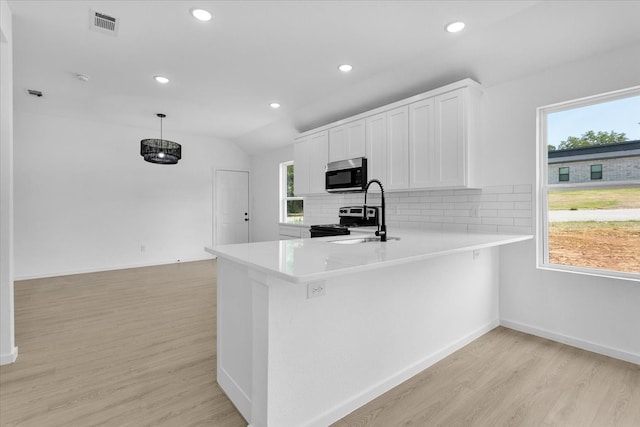 kitchen with a wealth of natural light, decorative backsplash, light hardwood / wood-style flooring, and stainless steel appliances