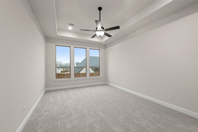 spare room with a raised ceiling, light carpet, ceiling fan, and baseboards