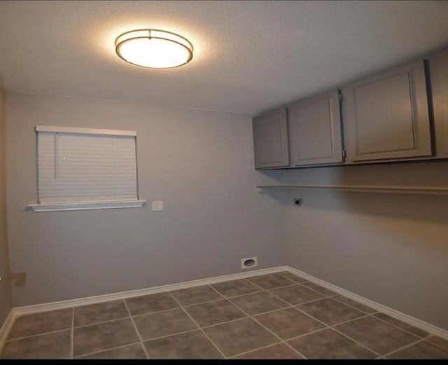 laundry room with a textured ceiling, electric dryer hookup, dark tile patterned floors, and cabinets