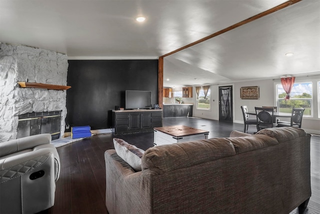 living room featuring dark hardwood / wood-style floors, vaulted ceiling, and a stone fireplace