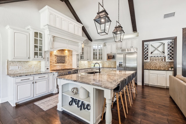 kitchen with built in appliances, sink, white cabinets, hanging light fixtures, and a center island with sink