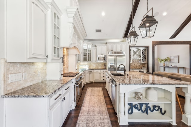 kitchen featuring a large island, built in appliances, sink, white cabinetry, and decorative light fixtures