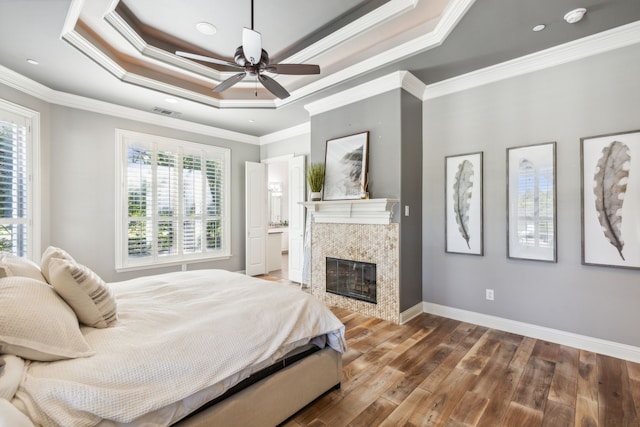 bedroom with multiple windows, wood-type flooring, a tiled fireplace, and ceiling fan