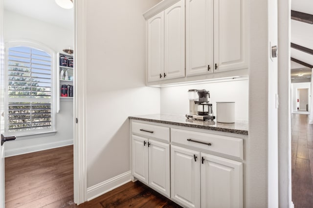 bar featuring dark stone counters, dark hardwood / wood-style floors, and white cabinets