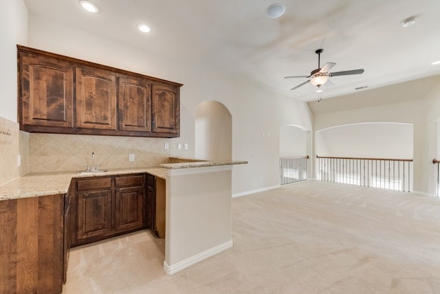 kitchen featuring light stone countertops, ceiling fan, decorative backsplash, and light carpet