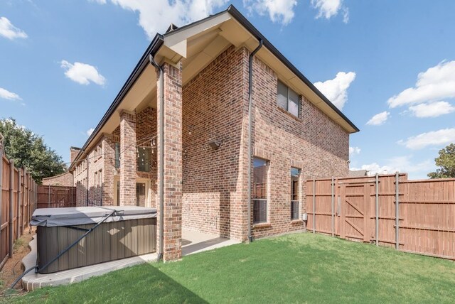 rear view of property with a hot tub and a lawn