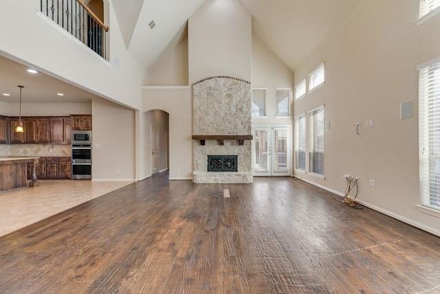 unfurnished living room with a stone fireplace, hardwood / wood-style flooring, and a towering ceiling