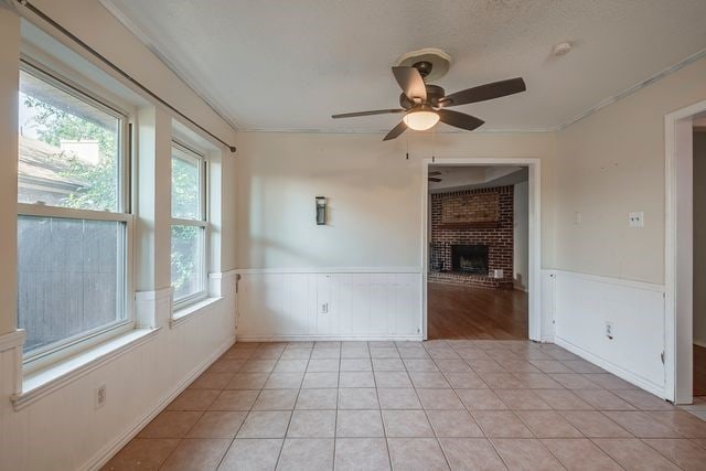 unfurnished room with light tile patterned floors, ceiling fan, wainscoting, and a fireplace