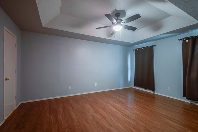 unfurnished bedroom with a ceiling fan, a tray ceiling, baseboards, and wood finished floors