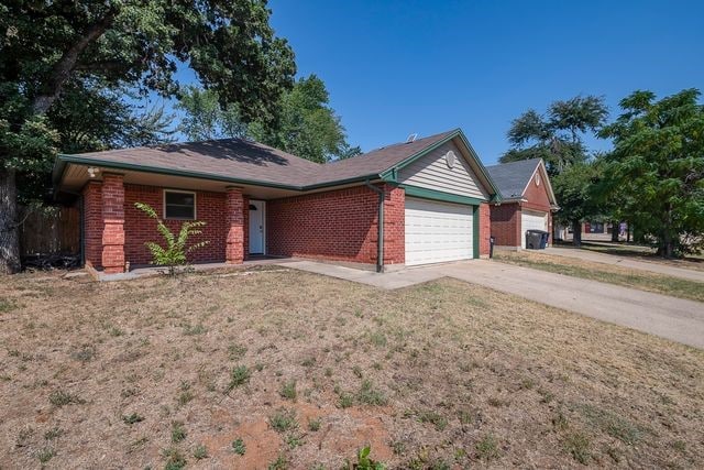 single story home featuring a garage, concrete driveway, brick siding, and a front yard