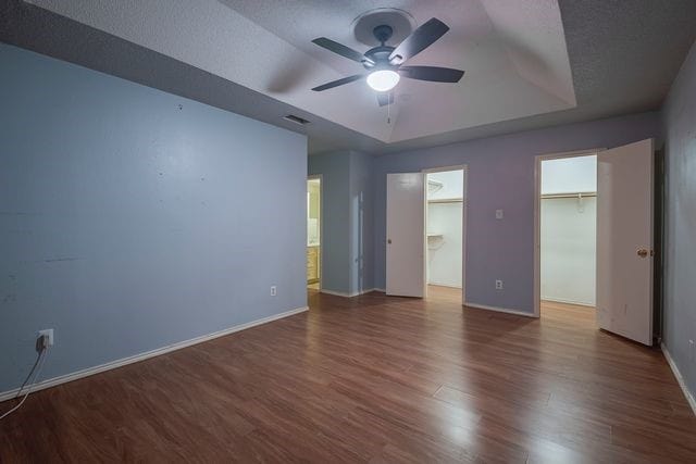 unfurnished bedroom featuring visible vents, baseboards, a raised ceiling, dark wood finished floors, and a spacious closet