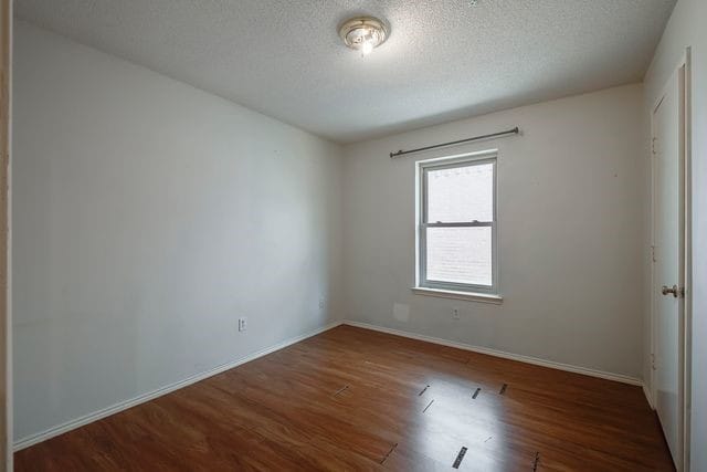 unfurnished room featuring a textured ceiling, baseboards, and wood finished floors