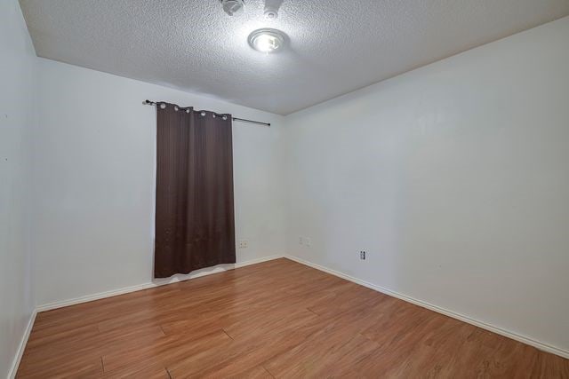 empty room featuring a textured ceiling, wood finished floors, and baseboards