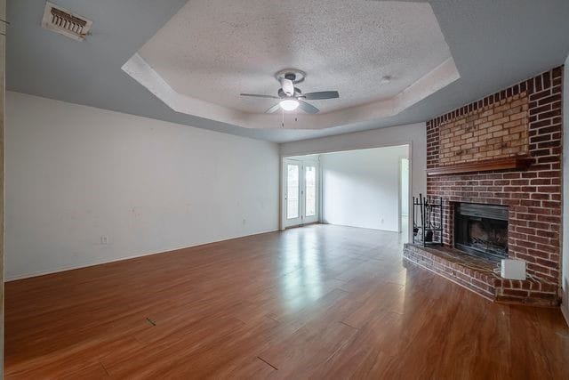 unfurnished living room with hardwood / wood-style floors, a raised ceiling, a fireplace, a textured ceiling, and ceiling fan