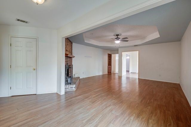 unfurnished living room featuring light wood finished floors, visible vents, a ceiling fan, a tray ceiling, and a fireplace