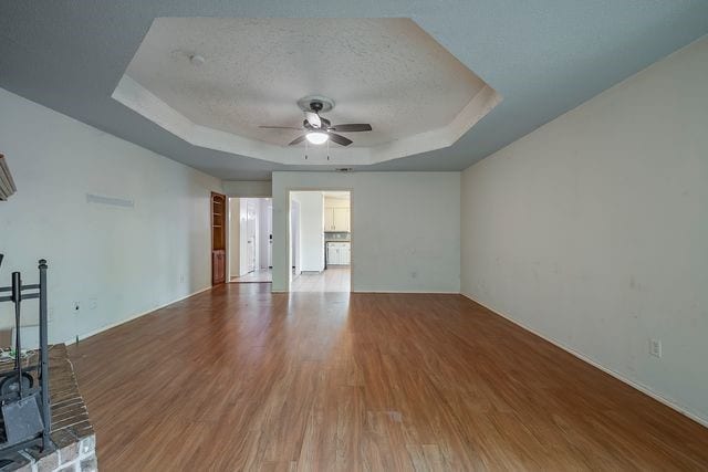 unfurnished living room featuring a tray ceiling, a wood stove, ceiling fan, a textured ceiling, and wood finished floors