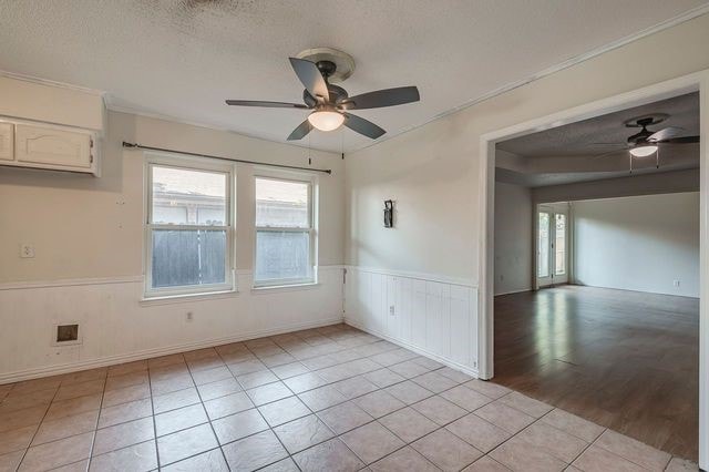 spare room with a textured ceiling, wainscoting, light tile patterned flooring, and a ceiling fan