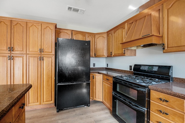 kitchen featuring custom exhaust hood, light hardwood / wood-style flooring, dark stone counters, and black appliances