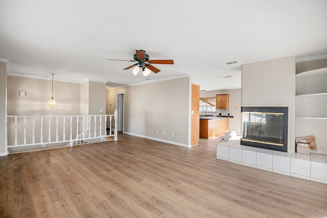 unfurnished living room with crown molding, light hardwood / wood-style flooring, a tile fireplace, and ceiling fan