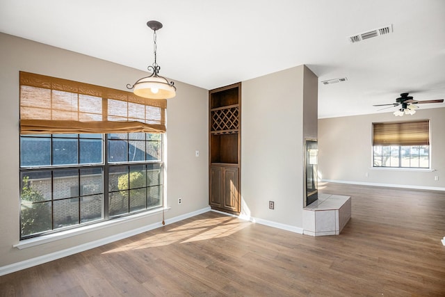 unfurnished living room featuring hardwood / wood-style flooring, a tile fireplace, ceiling fan, and built in shelves