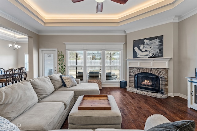 living room with dark hardwood / wood-style flooring, a fireplace, ceiling fan with notable chandelier, a raised ceiling, and crown molding