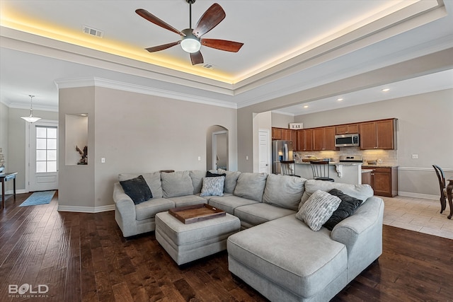 living room with ceiling fan, a raised ceiling, hardwood / wood-style flooring, and crown molding