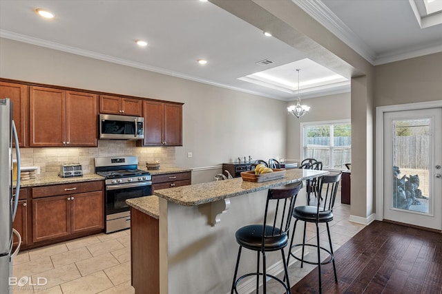 kitchen with light wood-type flooring, backsplash, a breakfast bar, appliances with stainless steel finishes, and light stone countertops