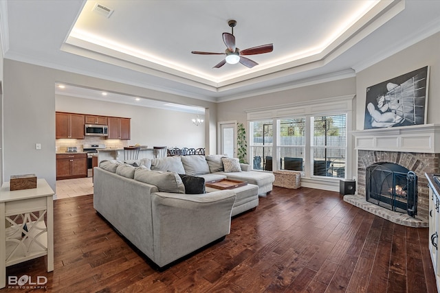 living room with a raised ceiling, a stone fireplace, and wood-type flooring