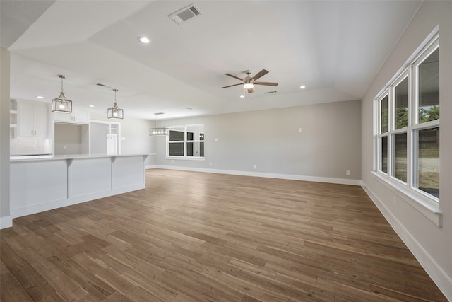 unfurnished living room with a raised ceiling, hardwood / wood-style floors, and ceiling fan