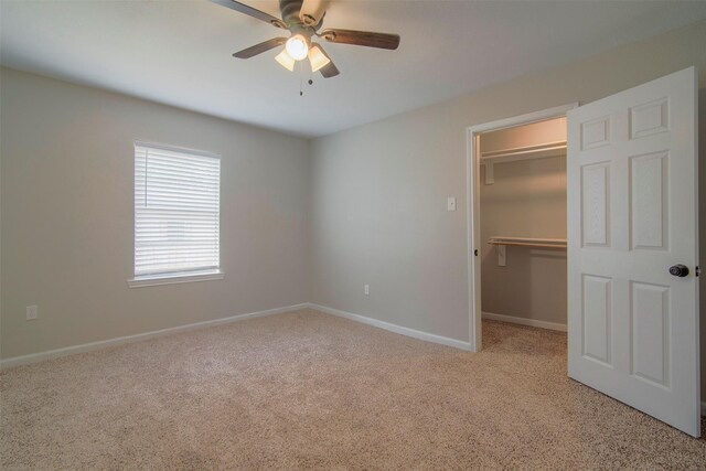 unfurnished bedroom with a walk in closet, a closet, ceiling fan, and light carpet