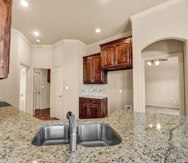 kitchen featuring light stone countertops, crown molding, and a sink