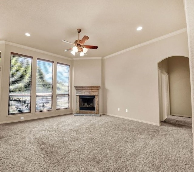 unfurnished living room with arched walkways, baseboards, a fireplace with raised hearth, crown molding, and carpet flooring