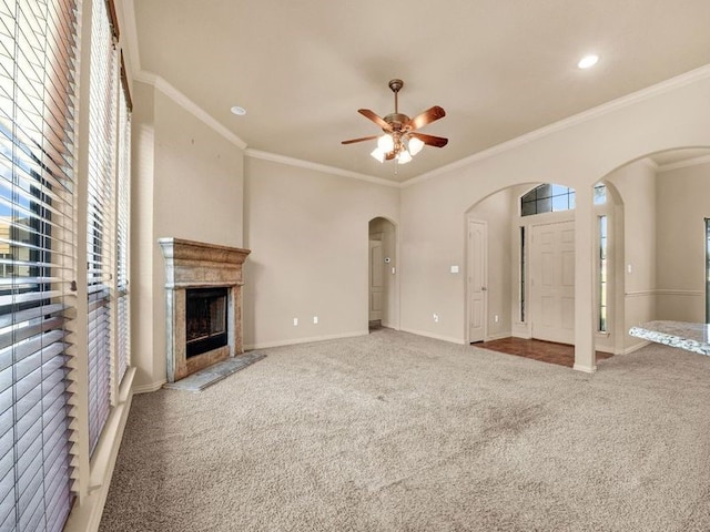 unfurnished living room with carpet floors, arched walkways, crown molding, a fireplace, and baseboards