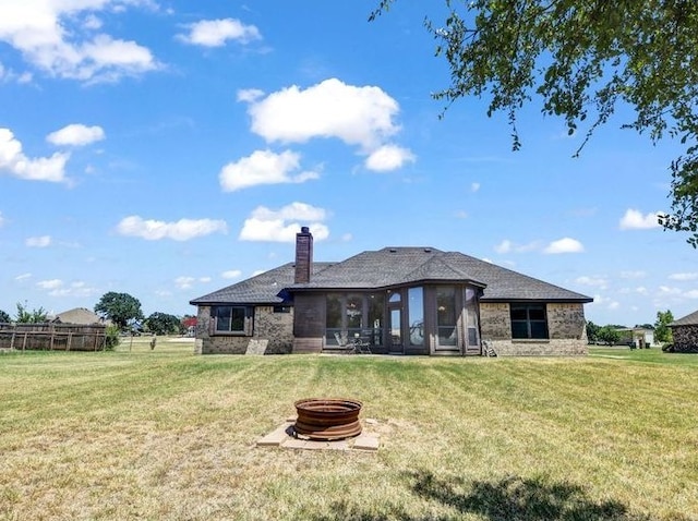 back of property with a yard, an outdoor fire pit, a chimney, and a sunroom