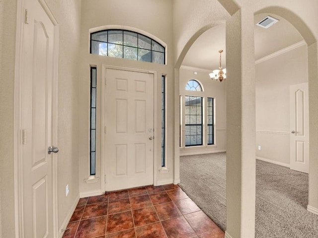 foyer entrance with arched walkways, crown molding, dark colored carpet, visible vents, and an inviting chandelier