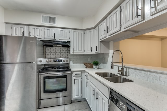 kitchen with light tile patterned flooring, backsplash, sink, light stone countertops, and stainless steel appliances