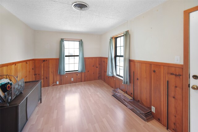 empty room featuring a textured ceiling, light hardwood / wood-style flooring, and wood walls