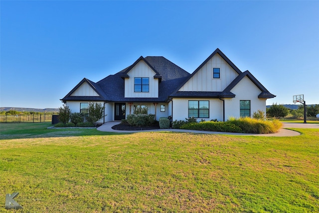 modern farmhouse style home featuring roof with shingles, fence, board and batten siding, and a front yard