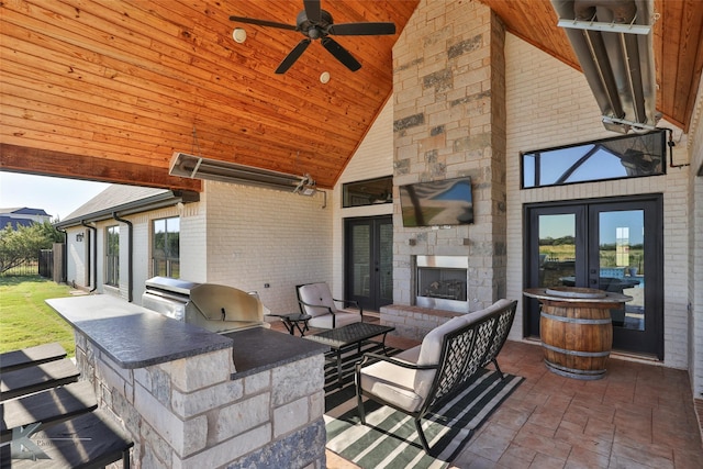 view of patio / terrace with an outdoor living space with a fireplace, ceiling fan, an outdoor kitchen, and french doors