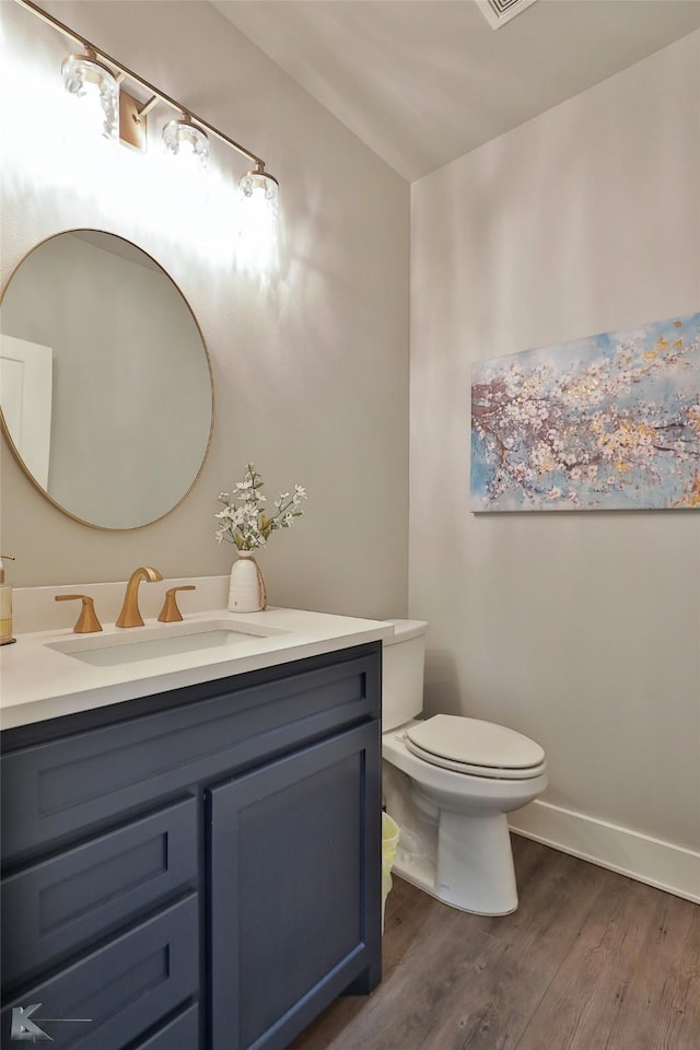 half bathroom with toilet, wood finished floors, visible vents, vanity, and baseboards