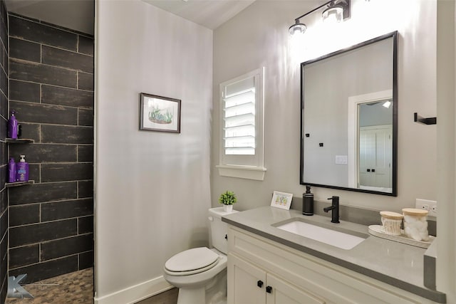 bathroom with a tile shower, vanity, and toilet