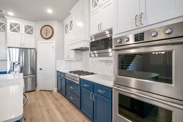 kitchen featuring appliances with stainless steel finishes, backsplash, light hardwood / wood-style floors, blue cabinets, and custom exhaust hood