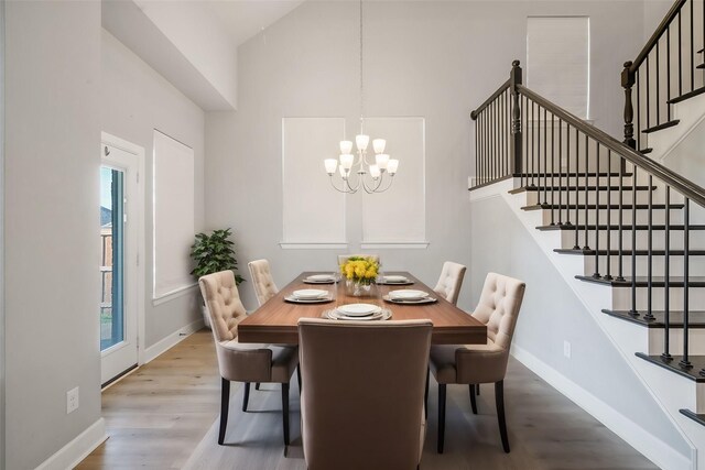 dining area featuring a towering ceiling, plenty of natural light, an inviting chandelier, and light wood-type flooring