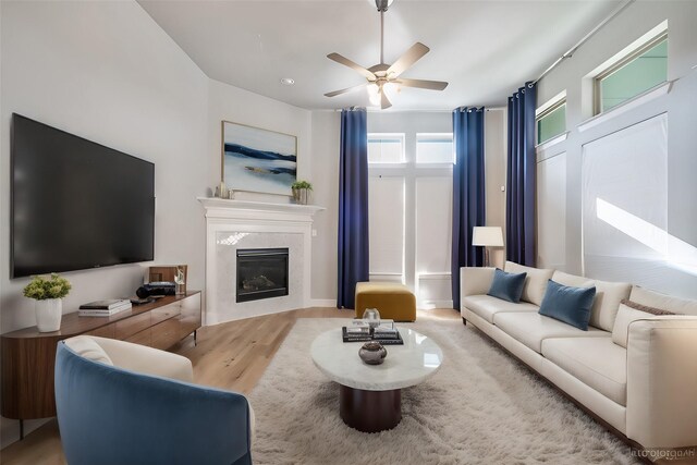 living room with light hardwood / wood-style floors, a premium fireplace, and ceiling fan