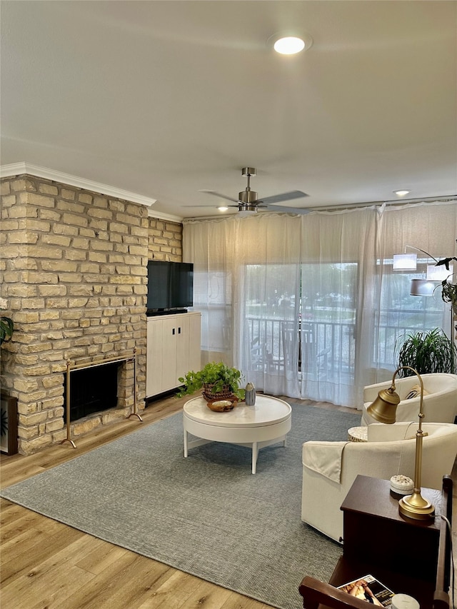 living room featuring hardwood / wood-style flooring, ceiling fan, a large fireplace, and crown molding