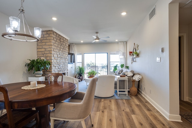 dining area featuring a fireplace, light hardwood / wood-style flooring, and ceiling fan with notable chandelier