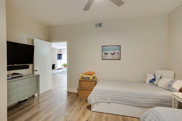 bedroom with a fireplace, light wood-type flooring, and ceiling fan