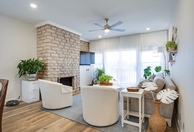 living room featuring ceiling fan, light hardwood / wood-style flooring, and a brick fireplace