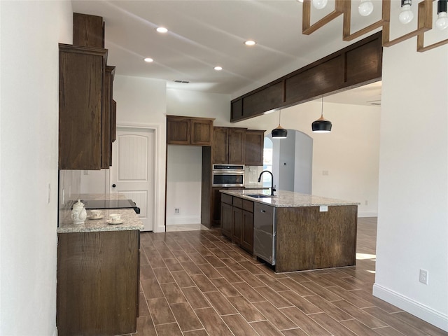 kitchen featuring light stone countertops, decorative light fixtures, oven, and sink